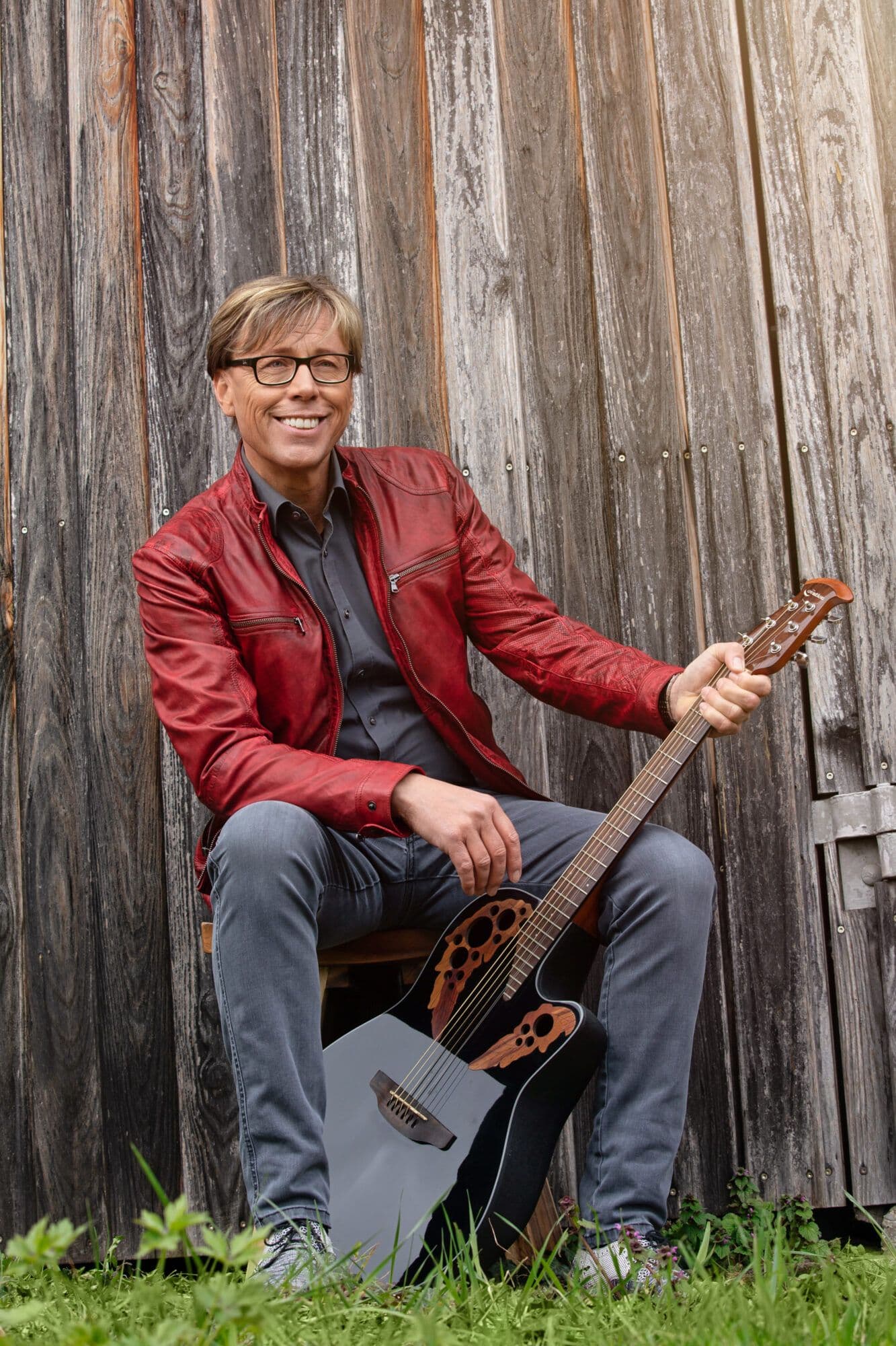 Hansy Vogt mit Gitarre vor einer Schwarzwälder Holzfassade